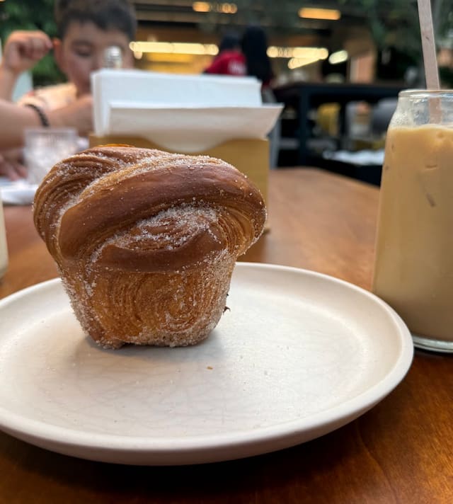 Cruffin azucarado sobre un plato de cerámica con café helado al fondo