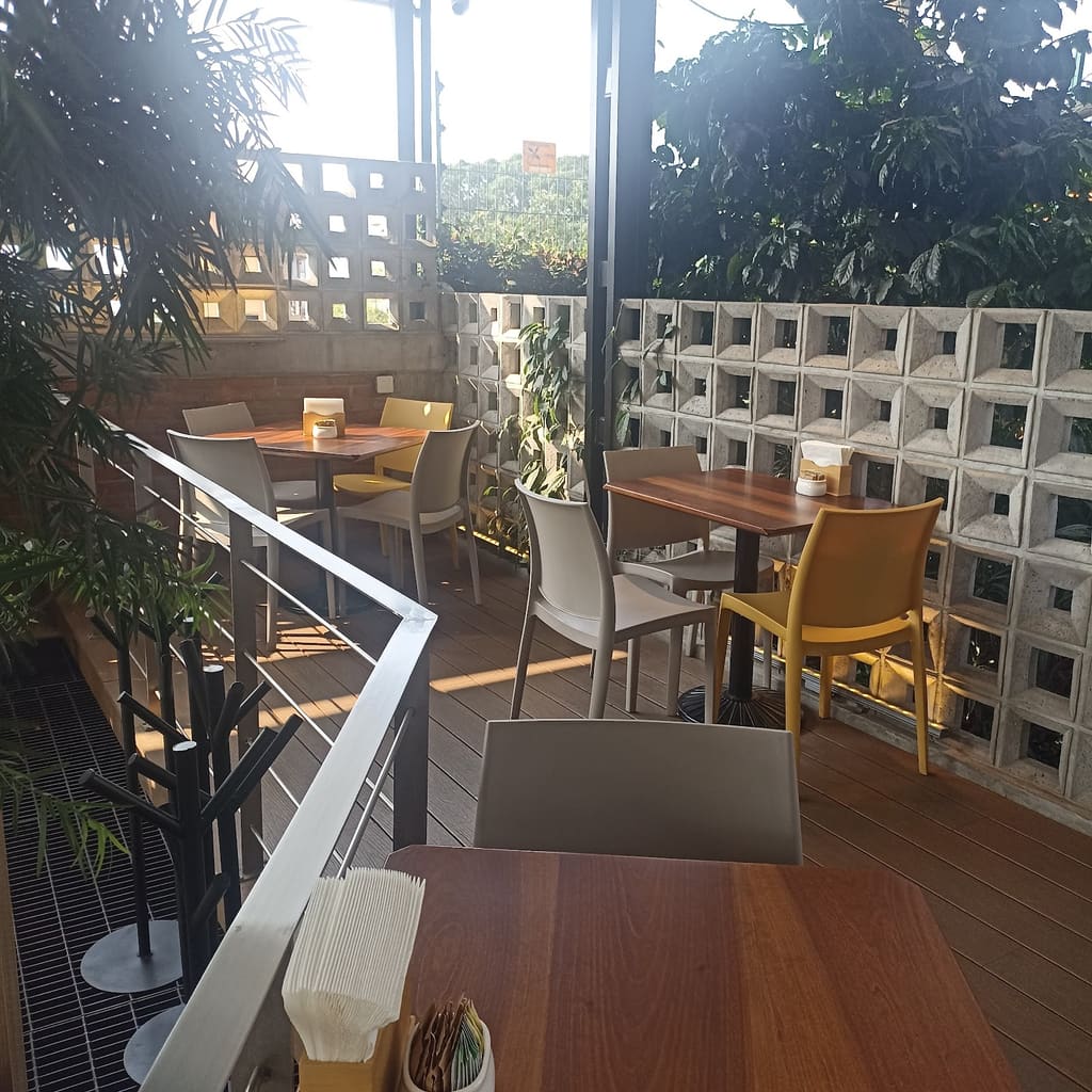 Terraza Miel: sillas amarillas y mesas de madera entre plantas, con muro de celosía
