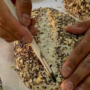 Manos del panadero greñando una hogaza de masa madre cubierta de semillas en Pan y Miel.